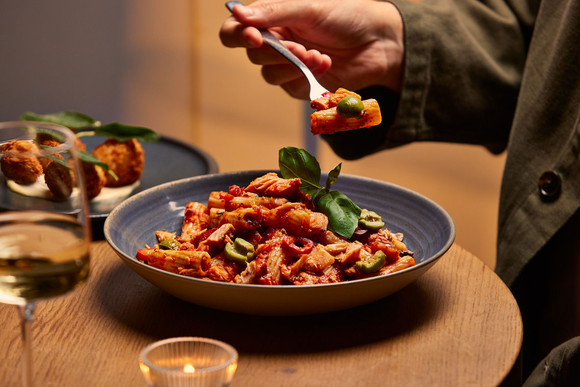 A person eating pasta with olives and basil