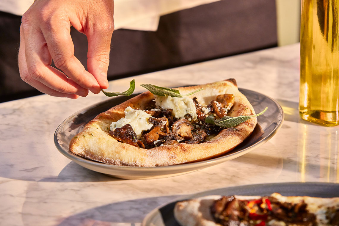 A chef finishing their bruschetta with fried sage leaves